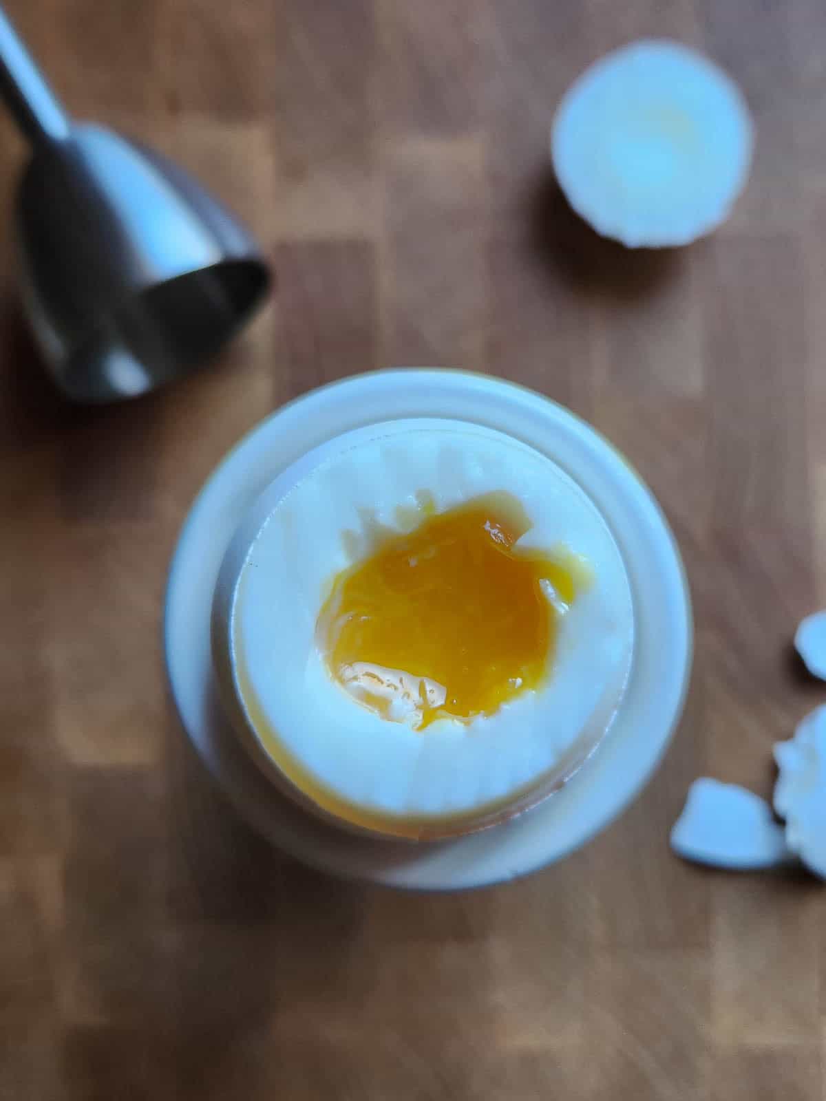 Overhead of the top of a soft boiled egg removed revealing a runny yolk.