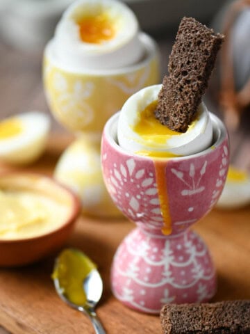 Close up of soft boiled eggs in pattered cups with toast in them.