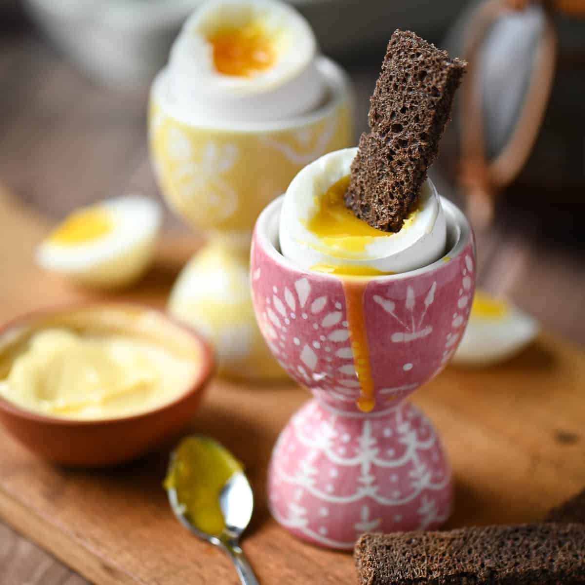 Eye level view of soft-boiled eggs in pink and yellow cups.