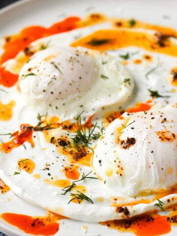 Two eggs on a white dish with chili butter on top with fresh dill.
