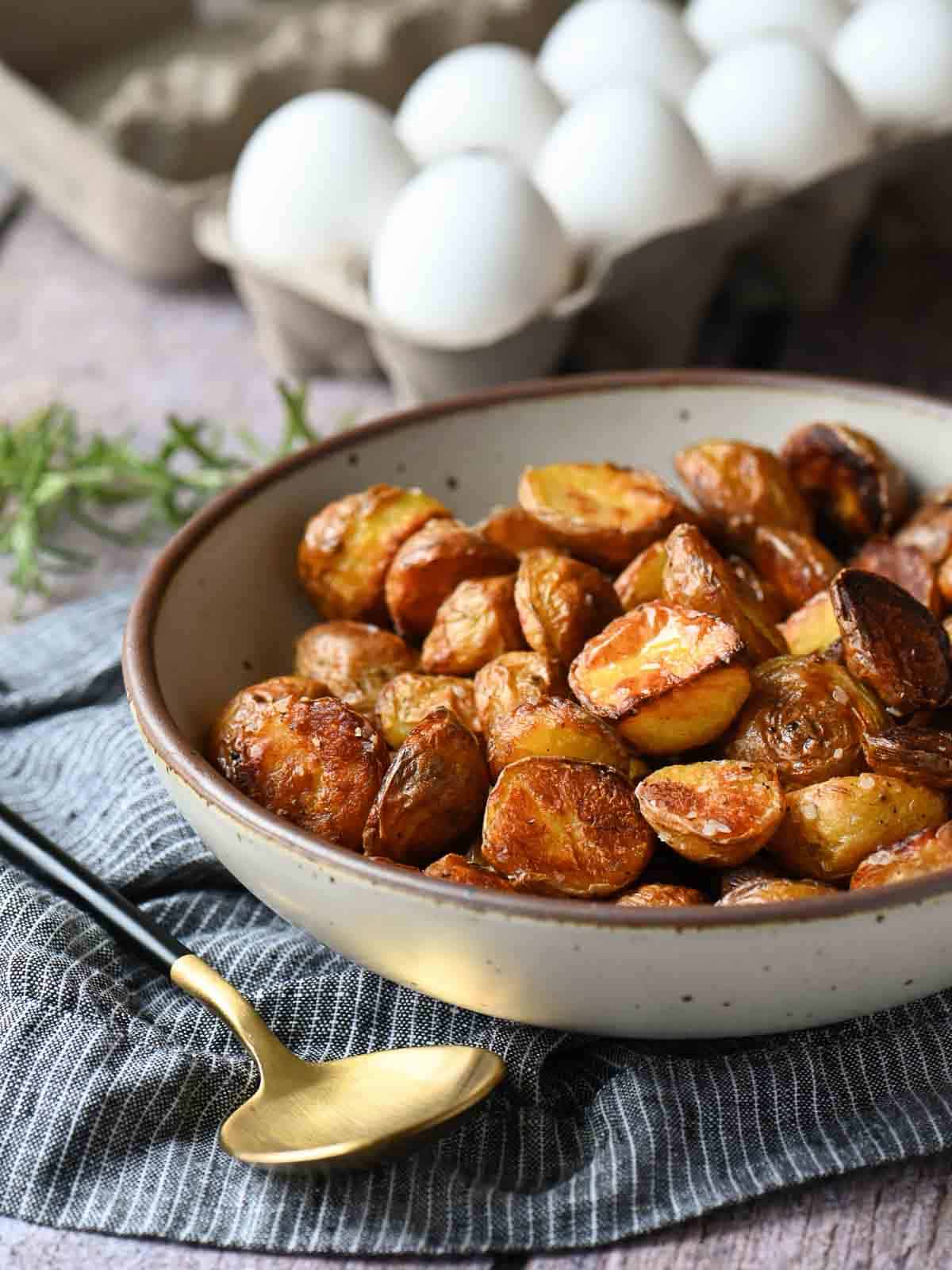 Roasted potatoes in a beige bowl with a spoon to the left.