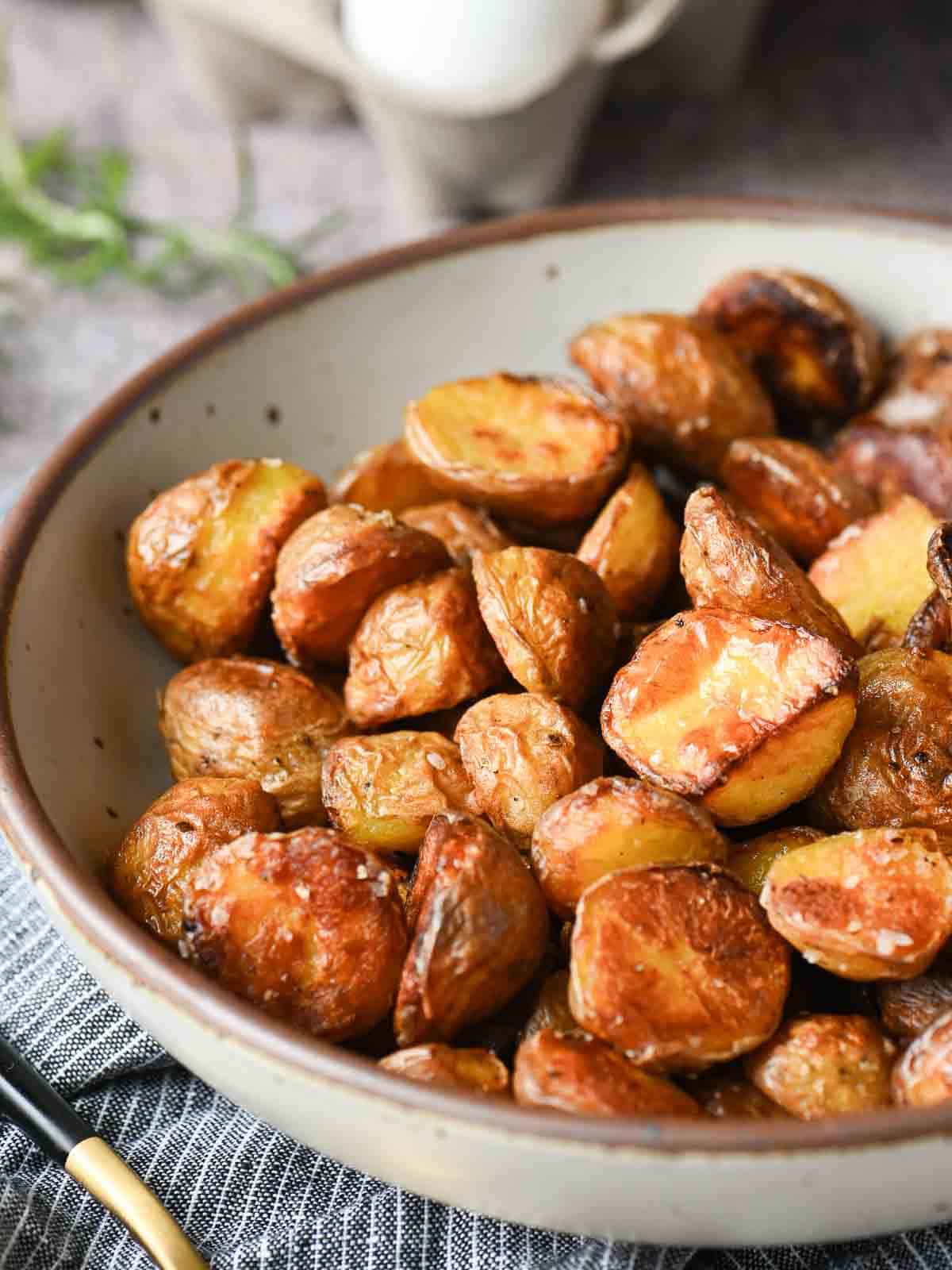 Close up of roasted potatoes in a beige bowl.