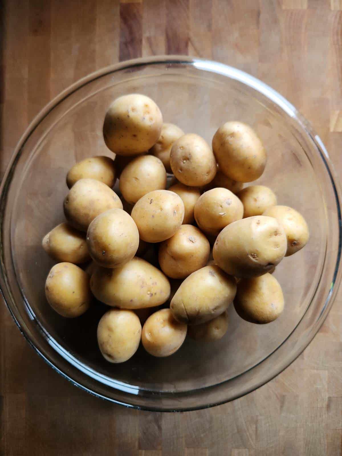 Raw whole potatoes in a clear bowl.
