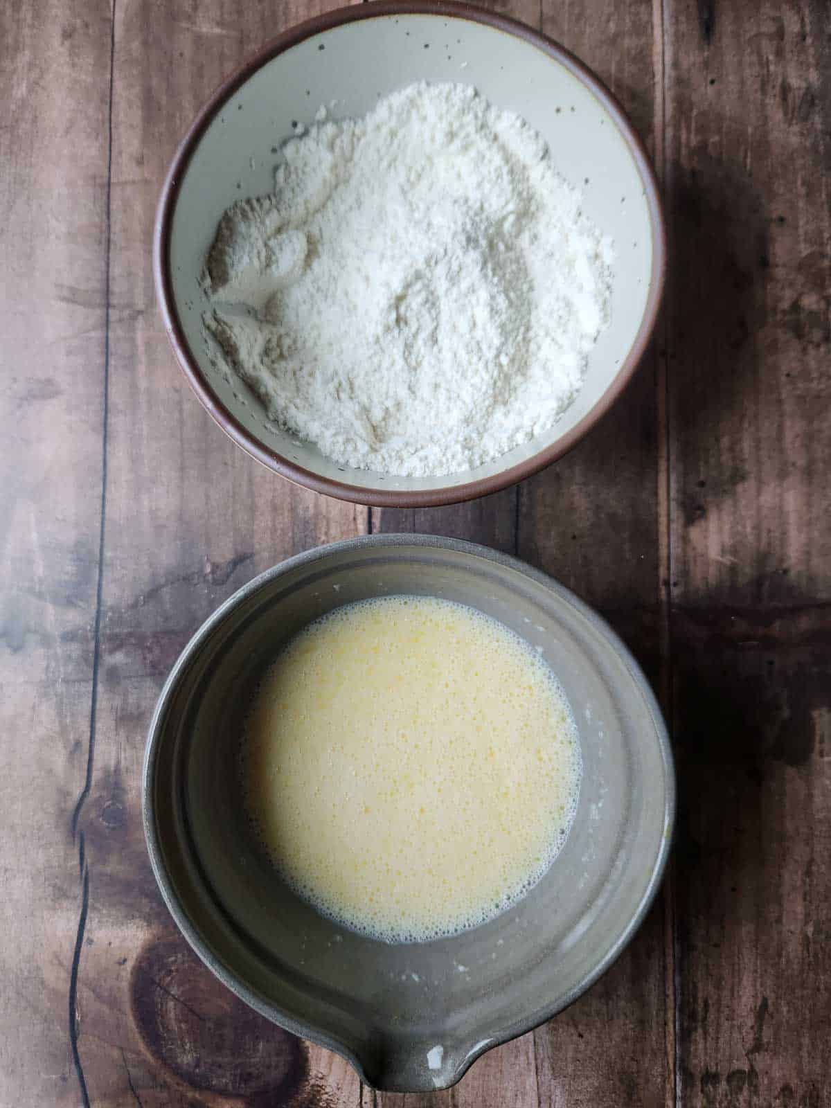 Overhead view of two bowls with dry and wet ingredients for waffle batter.
