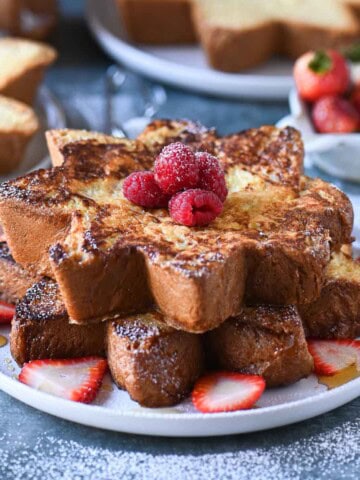 A stack of French toast with berries on a white plate on a blue surface.