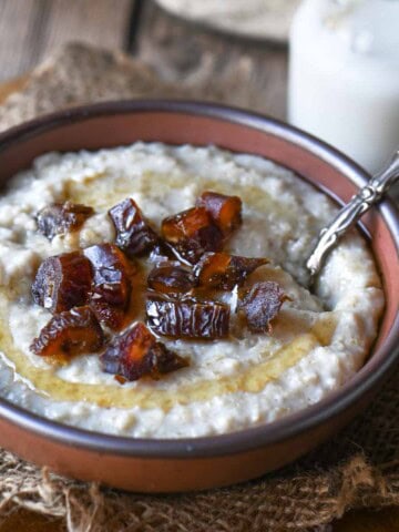 A bowl of oatmeal with honey and dates with a spoon to the right.
