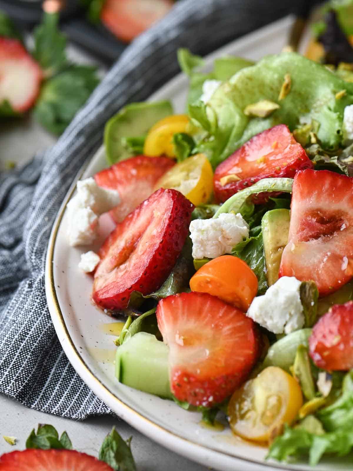 Close up of strawberries in a salad in a beige plate.