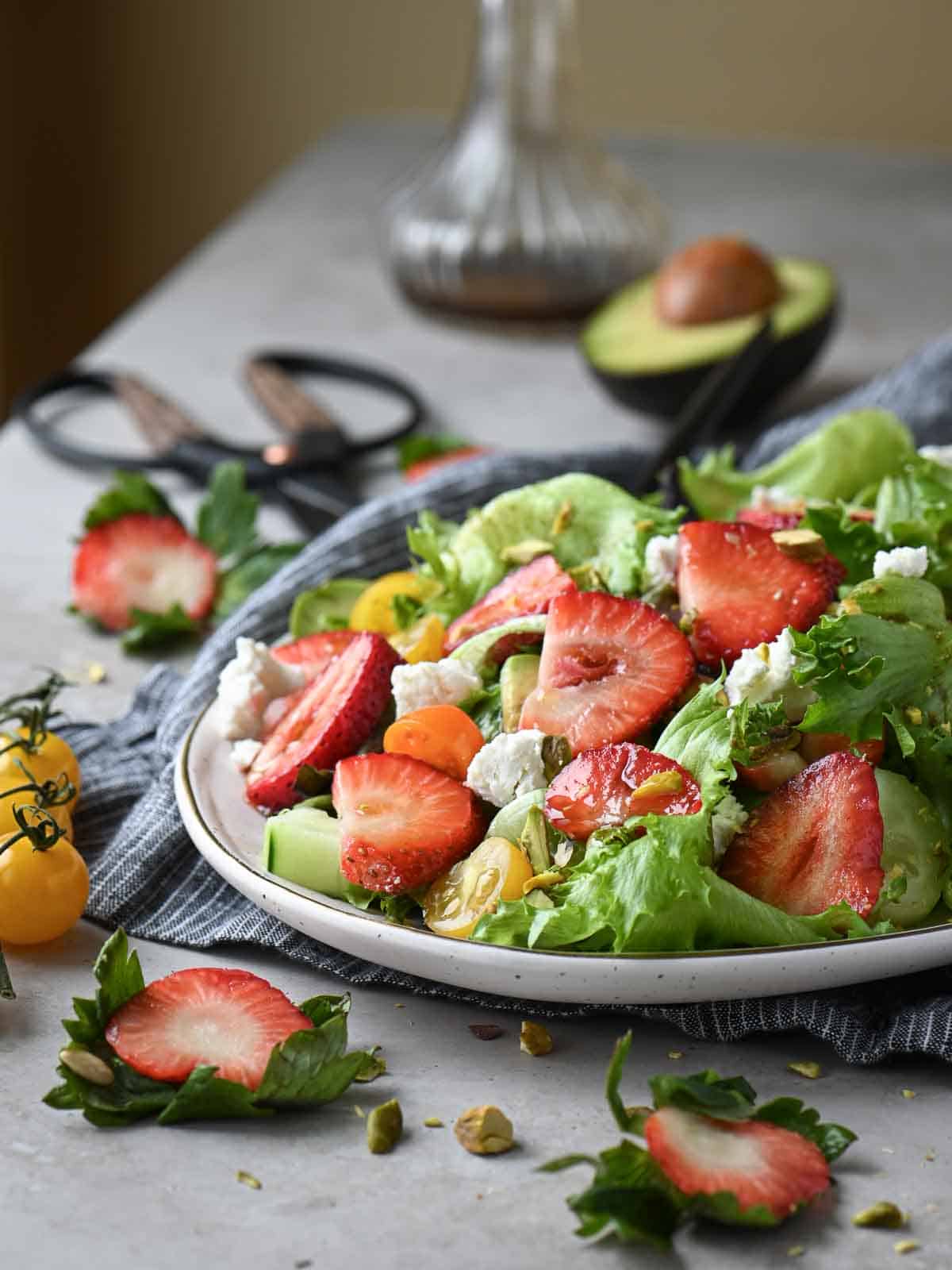 Strawberry salad with vegetables on a table with cut up fruit around it.