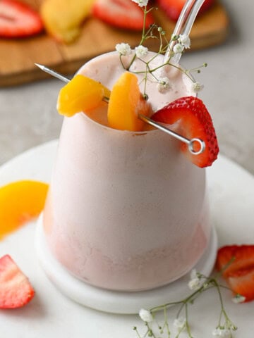 Angled view of a strawberry peach smoothie in a clear glass.