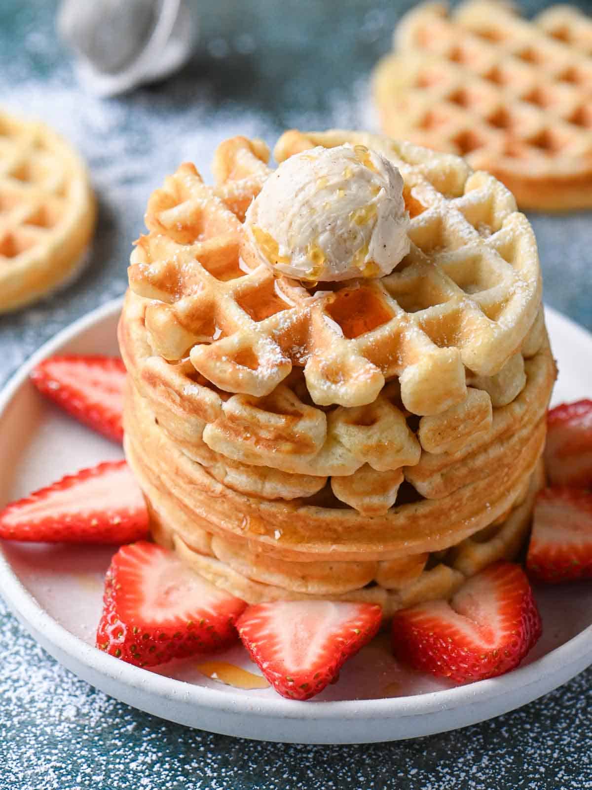 A stack of waffles with butter and powdered sugar on a blue surface.