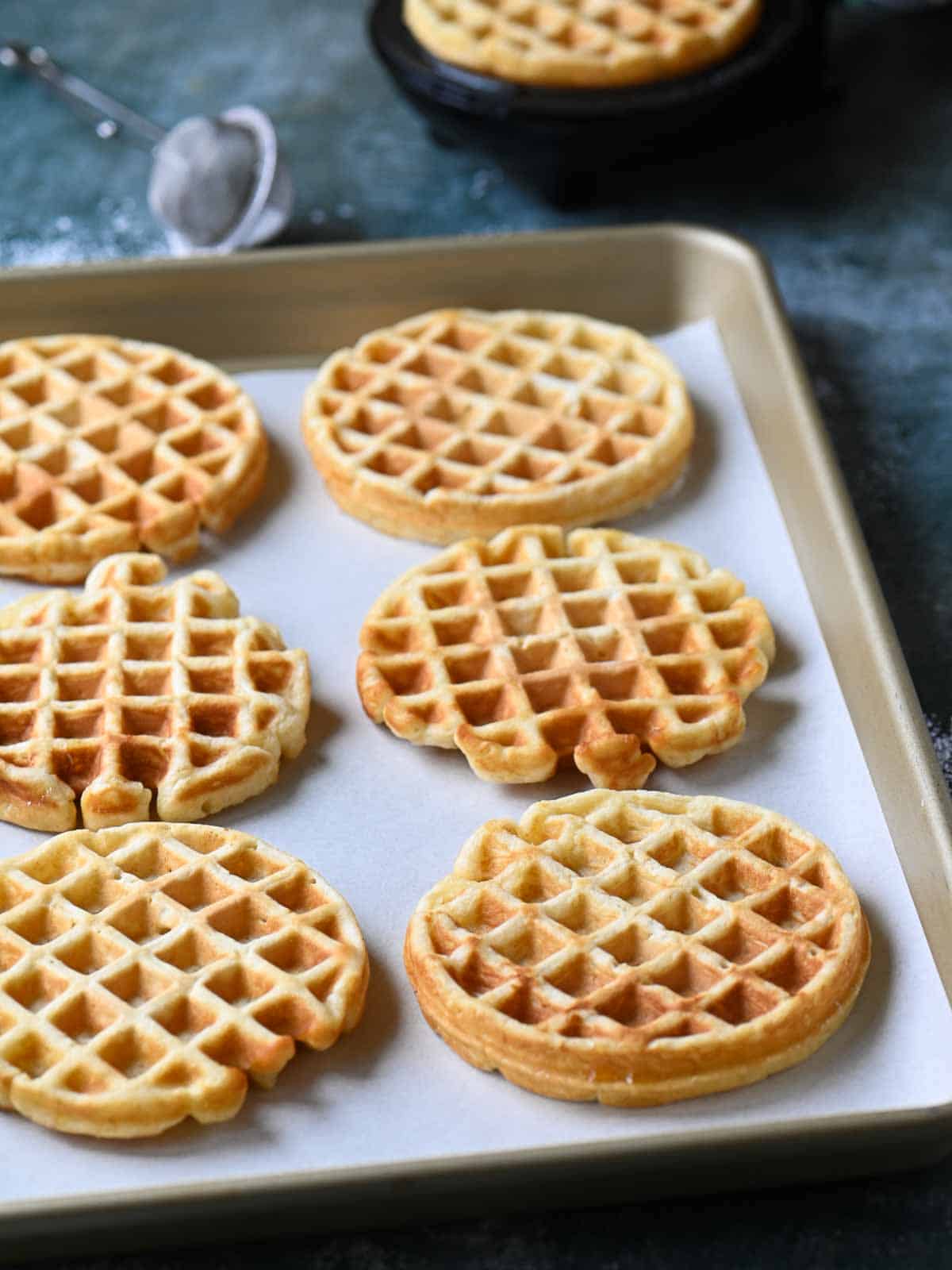 Six cooked waffles on a baking tray.