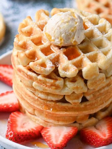 A stack of waffles on a white plate with strawberries.