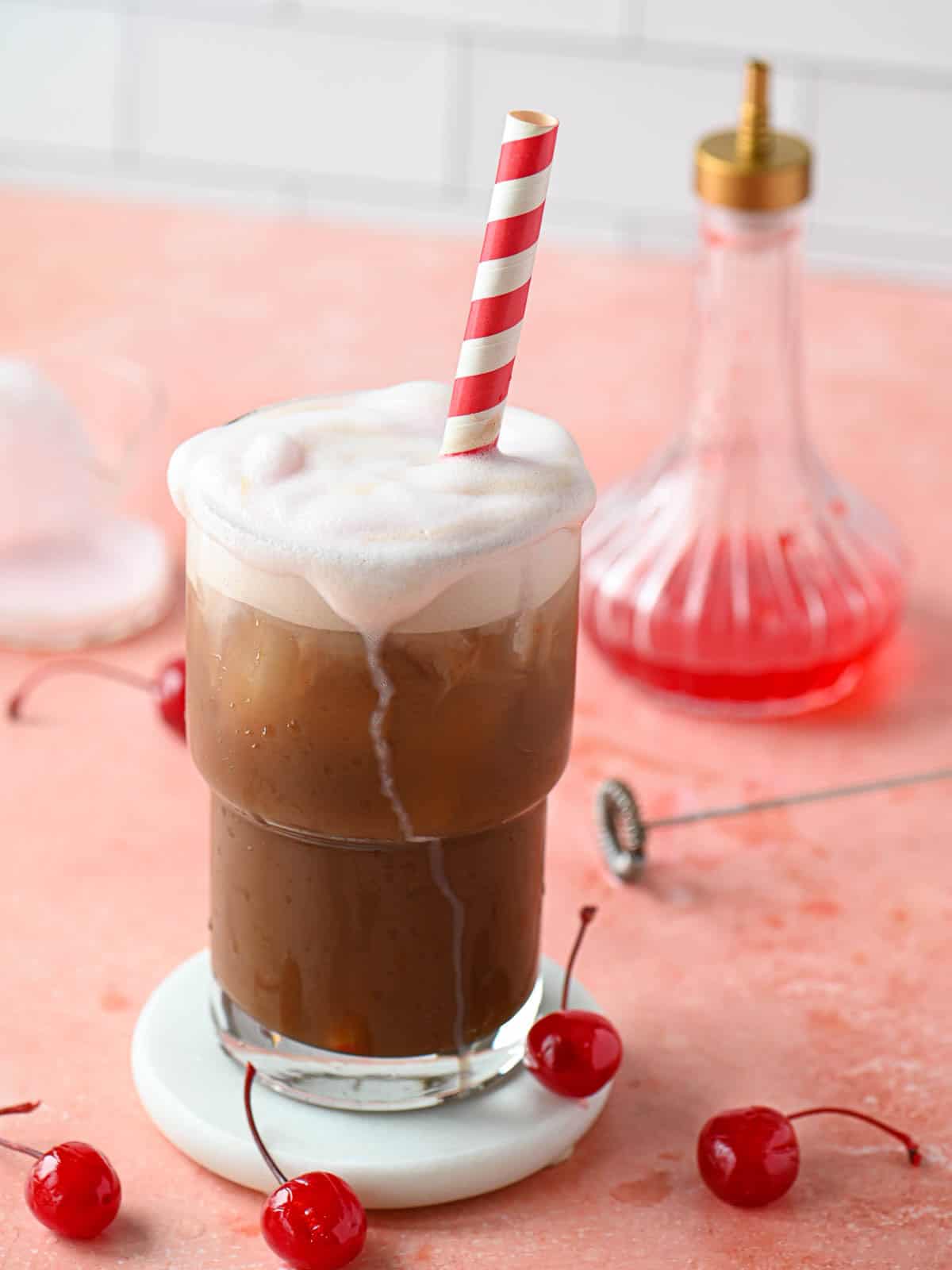 A cherry americola drink with cherry cold foam dripping down in a clear glass.