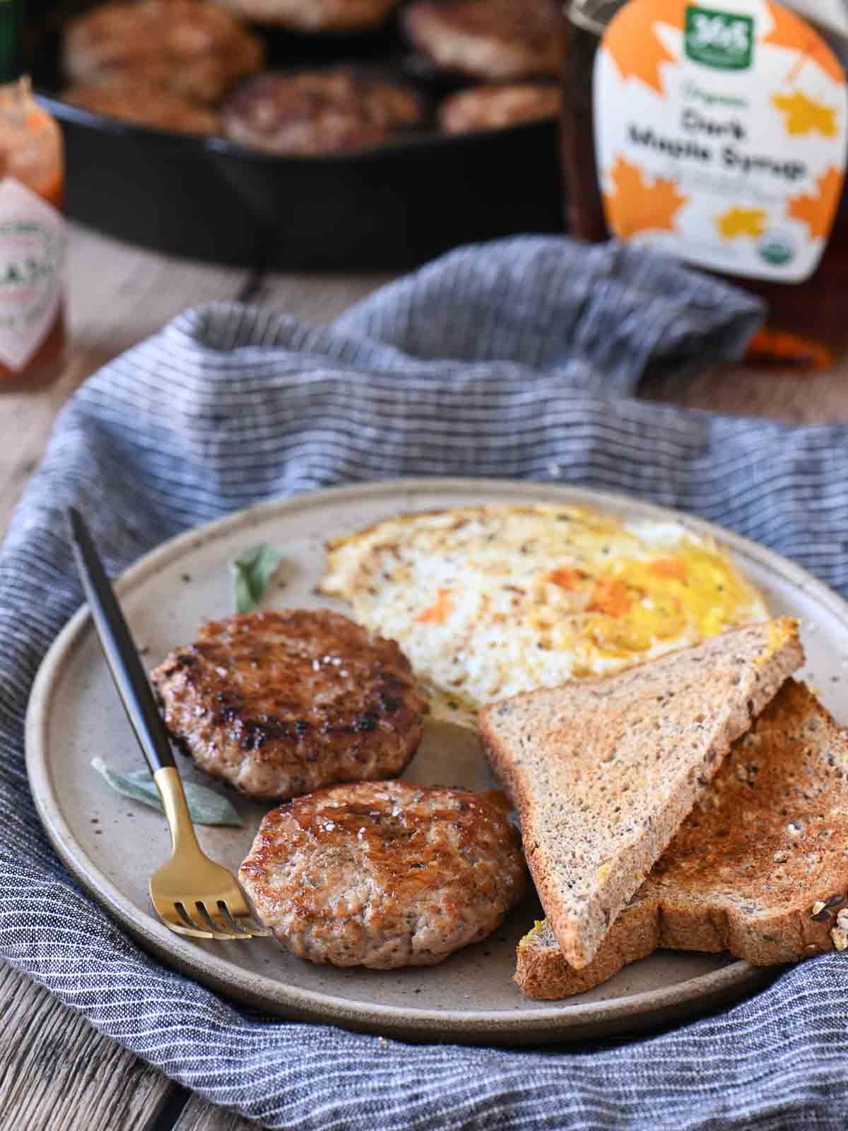 Angled view of sausage patties, eggs, and toast on a beige plate with a fork to the left.