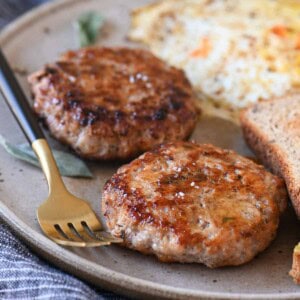 Two sausage patties on a beige plate with eggs and toast.