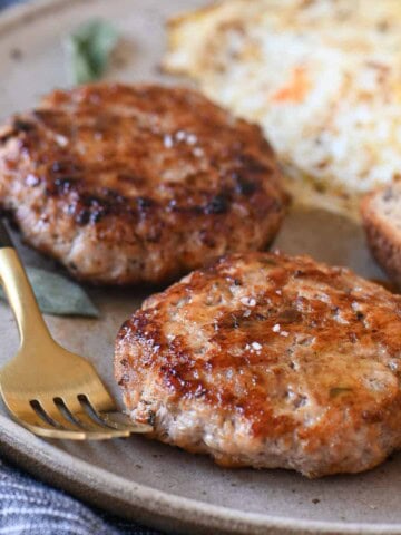 Two sausage patties on a beige plate with eggs and toast.