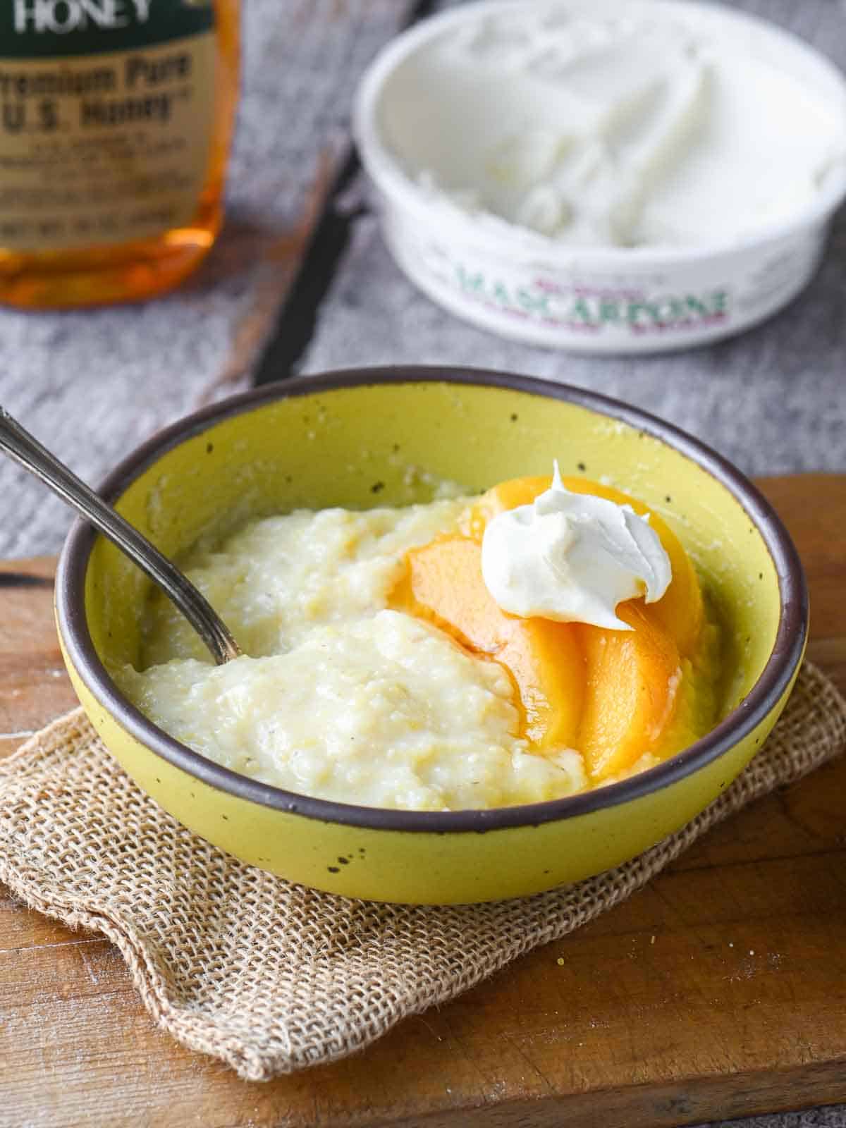 Creamy polenta in a yellow bowl with peaches and mascarpone.