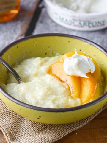Creamy polenta in a yellow bowl with peaches and mascarpone.