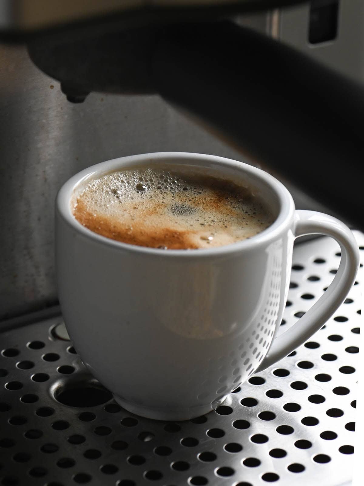 A white cup of espresso just pulled from an espresso machine.
