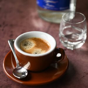 Espresso in a brown coffee cup with a shot glass to the right.