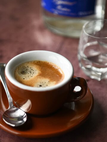 Espresso in a brown coffee cup with a shot glass to the right.