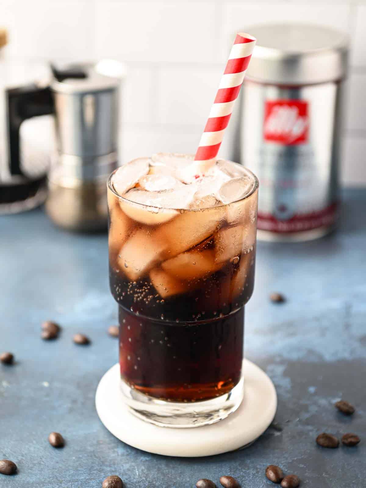 A clear glass of espresso soda on a blue surface.