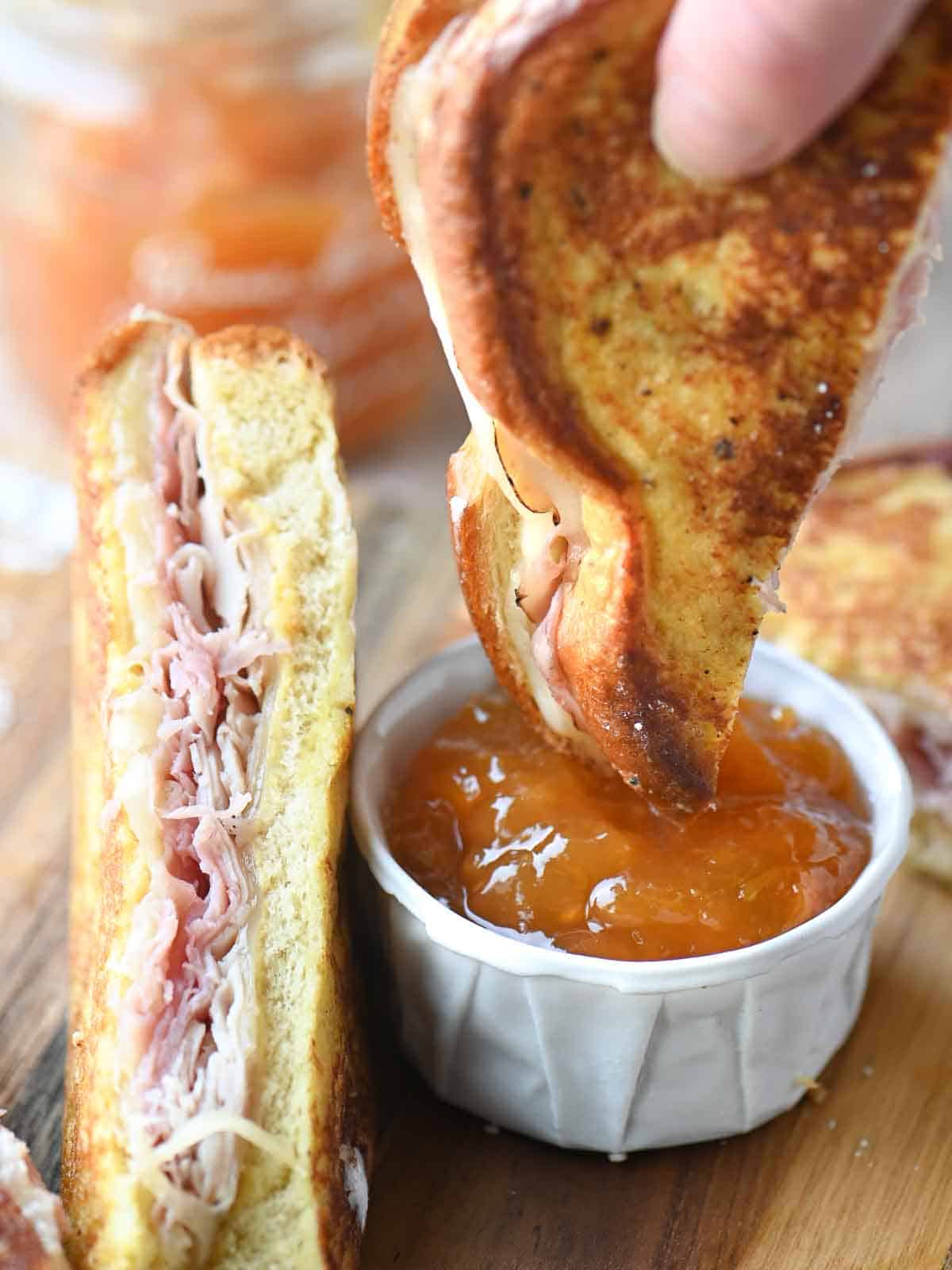 A Monte Cristo sandwich being dunked into apricot jam.
