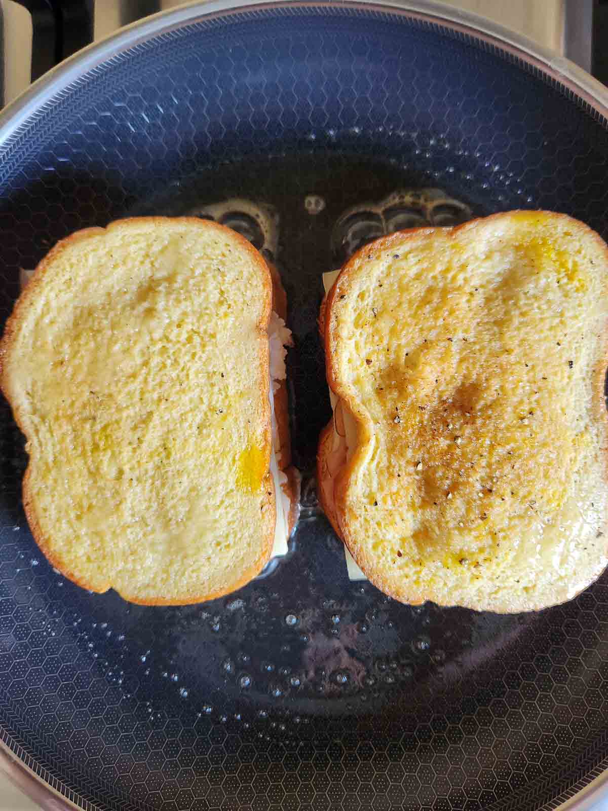 Overhead of two Monte Cristo sandwiches in a frying pan with butter.