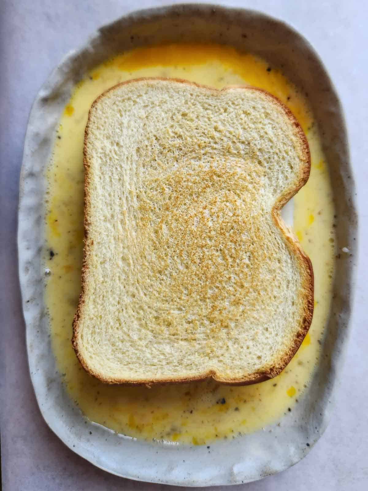 Overhead of a sandwich being dipped in egg custard.
