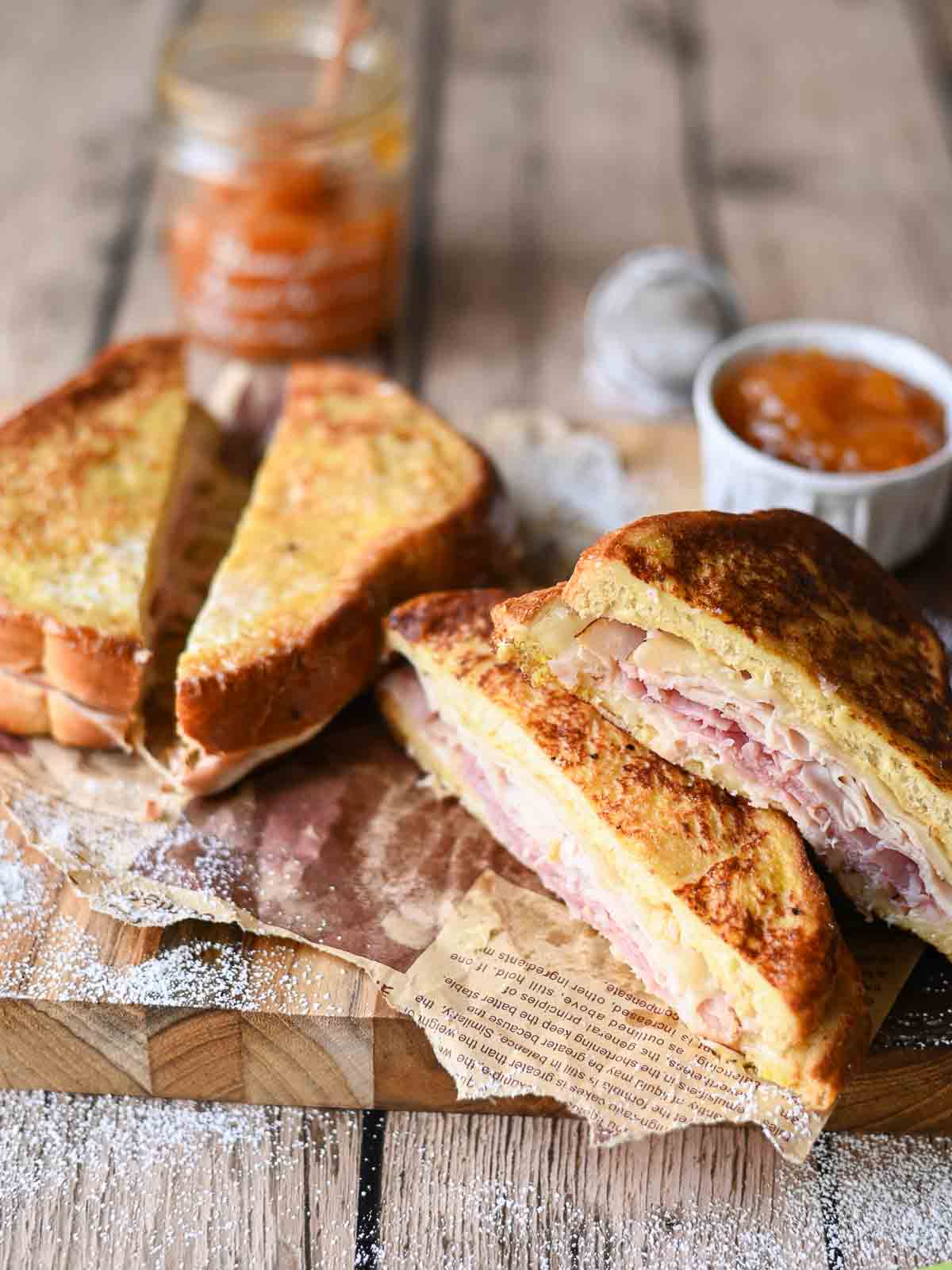 Monte Cristo sandwiches on a wooden board with apricot jam cut open.