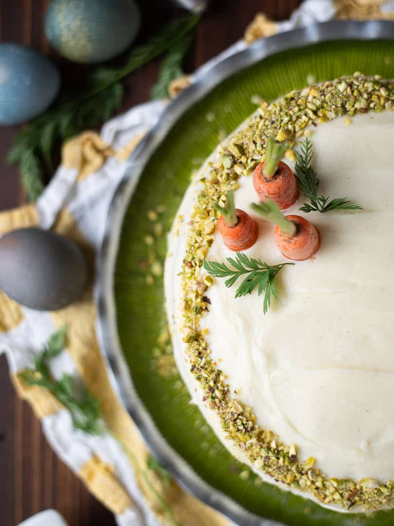 Overhead of pistachio carrot cake on a green platter with 3 carrots.