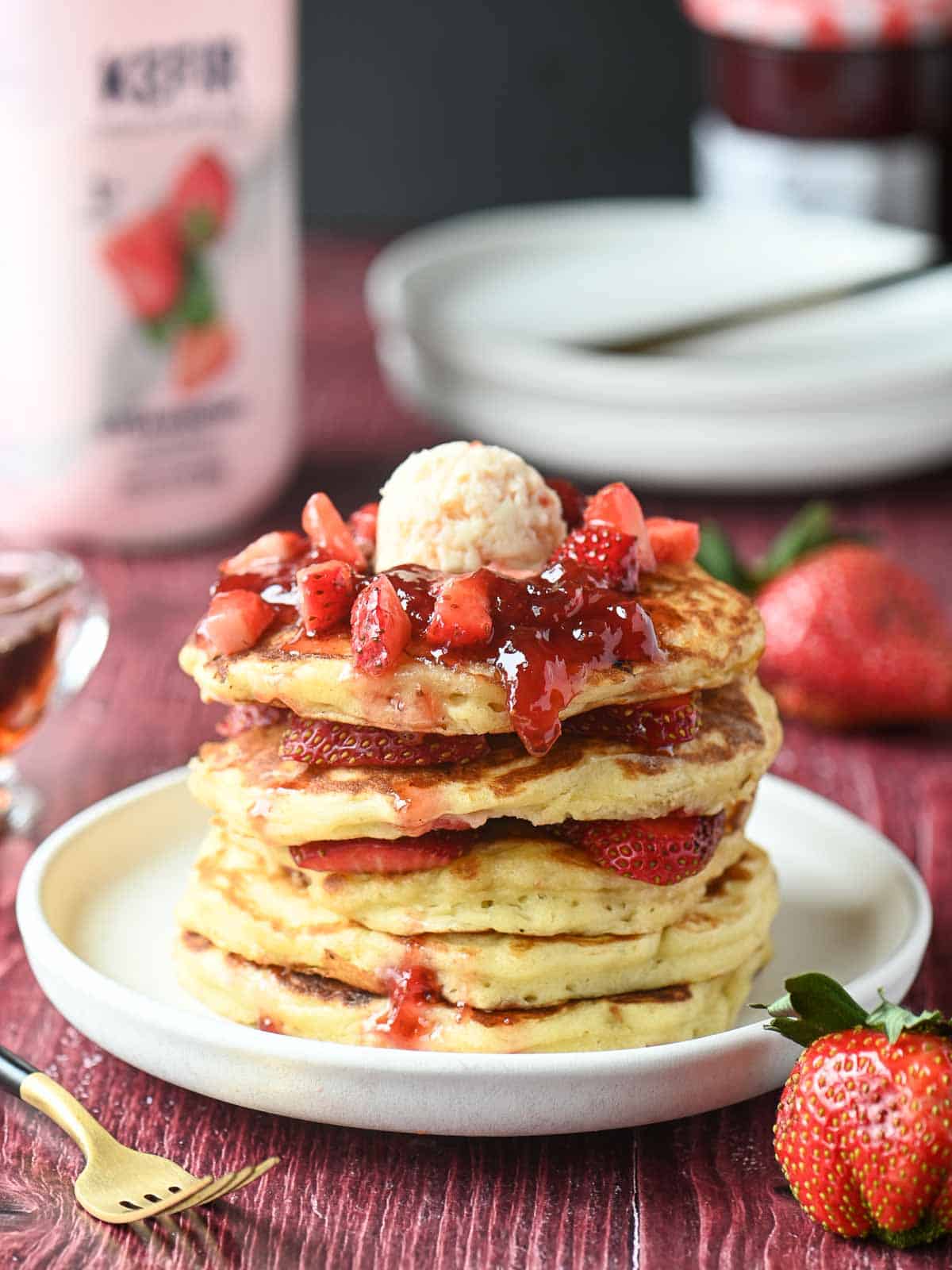 An eye-level view of a stack of strawberry kefir pancakes with jammy strawberries on top.