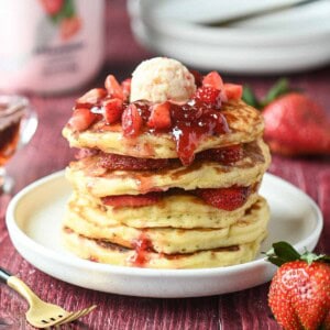 A stack of strawberry kefir pancakes with jammy strawberries on top.