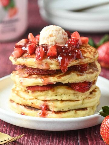 A stack of strawberry kefir pancakes with jammy strawberries on top.