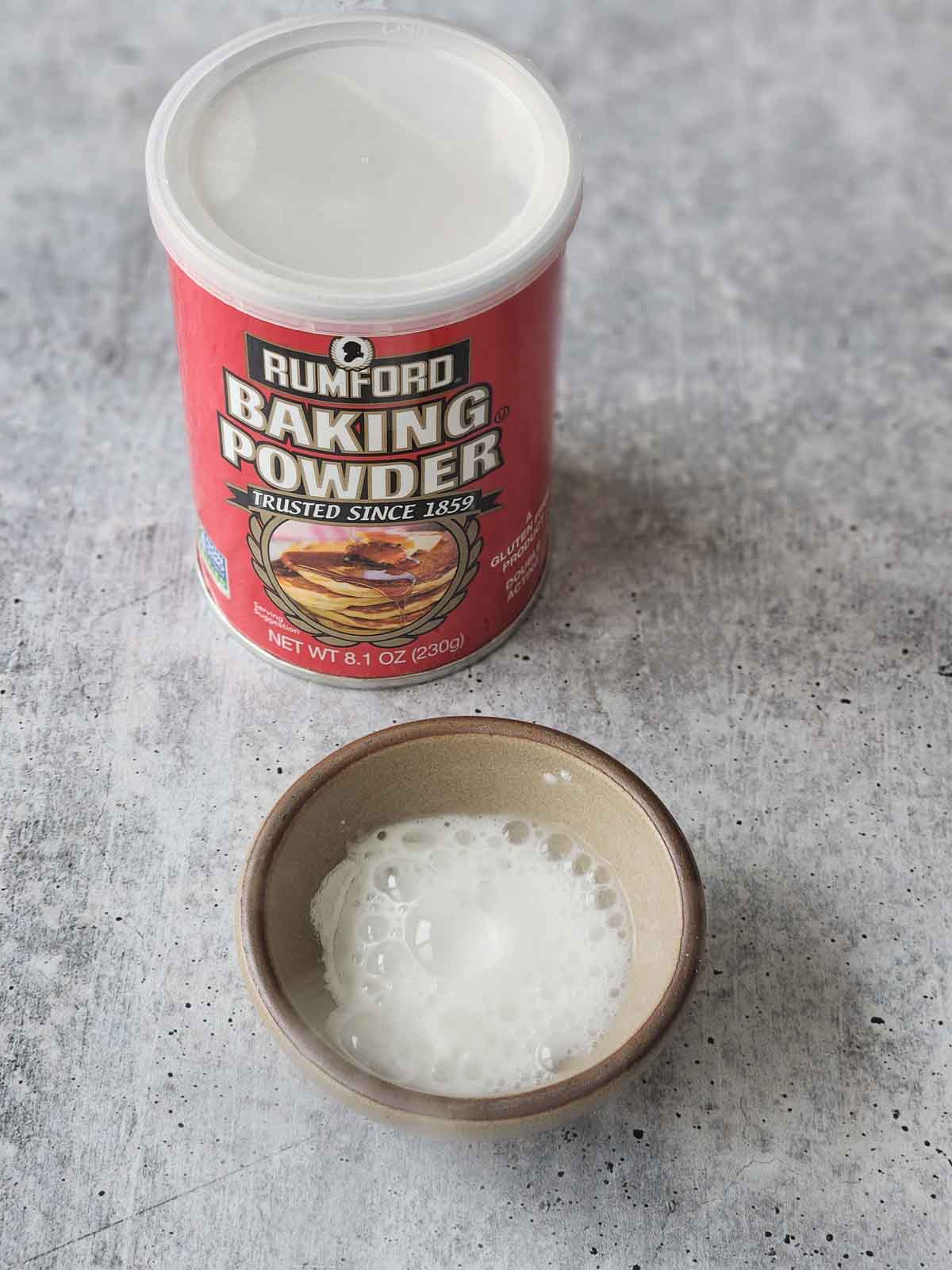 Baking powder bubbling in a bowl with water on a grey surface.