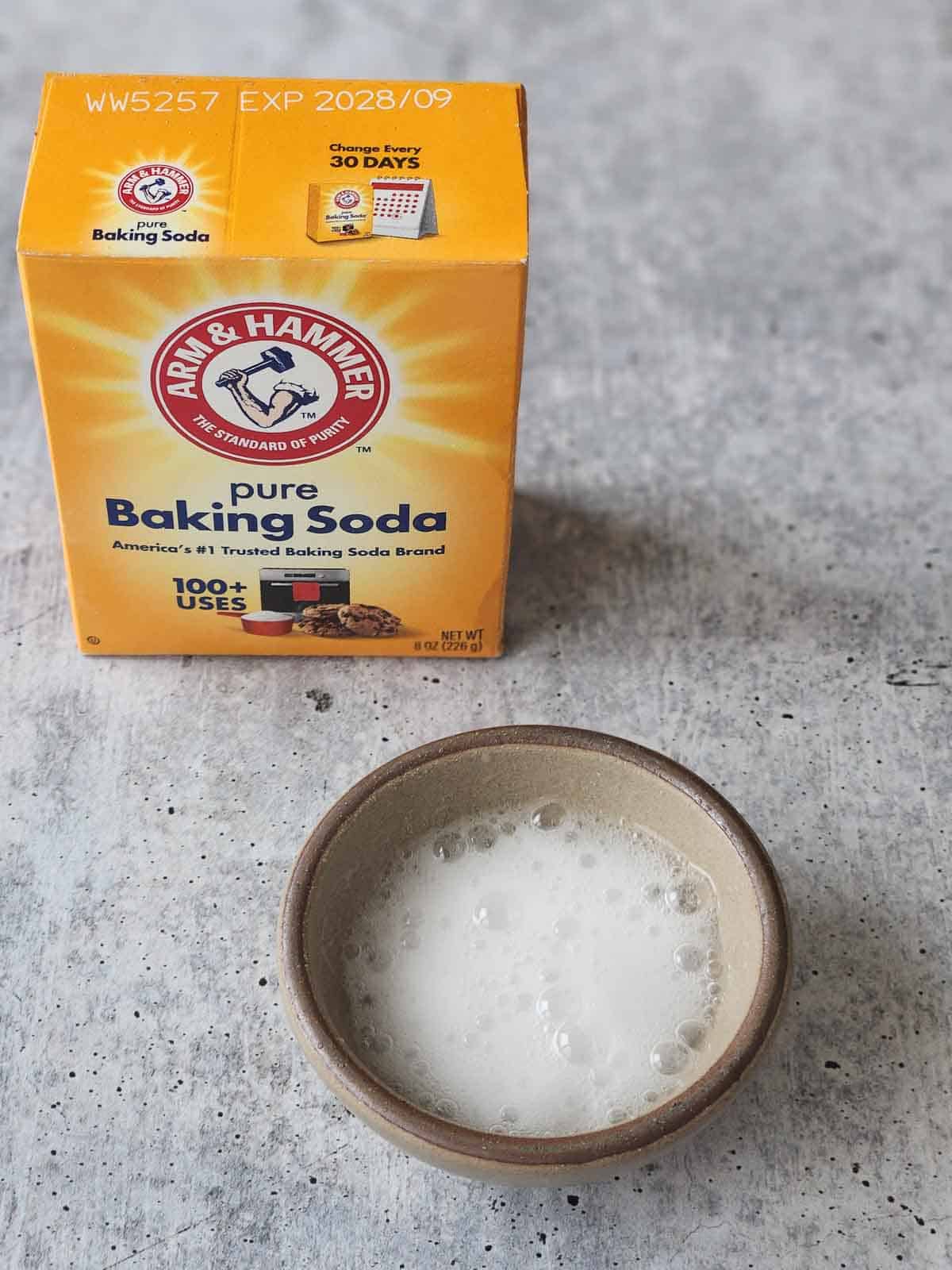 Baking soda bubbling in a small bowl on a grey surface.