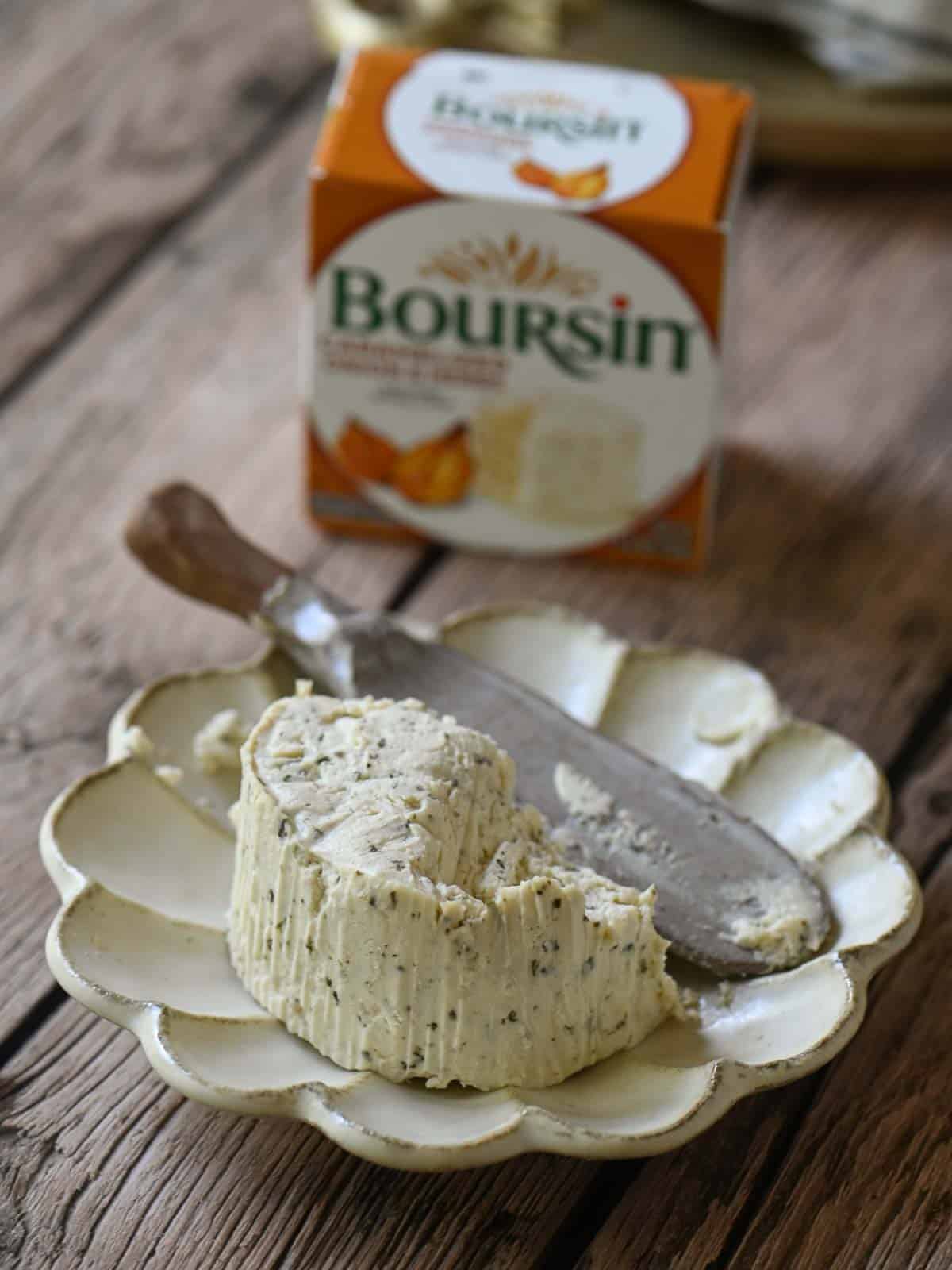 A close-up of Boursin cheese on a scalloped plate with a spreader.