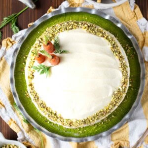 Overhead of a pistachio carrot cake on a green plate with carrots on top.