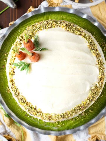 Overhead of a pistachio carrot cake on a green plate with carrots on top.