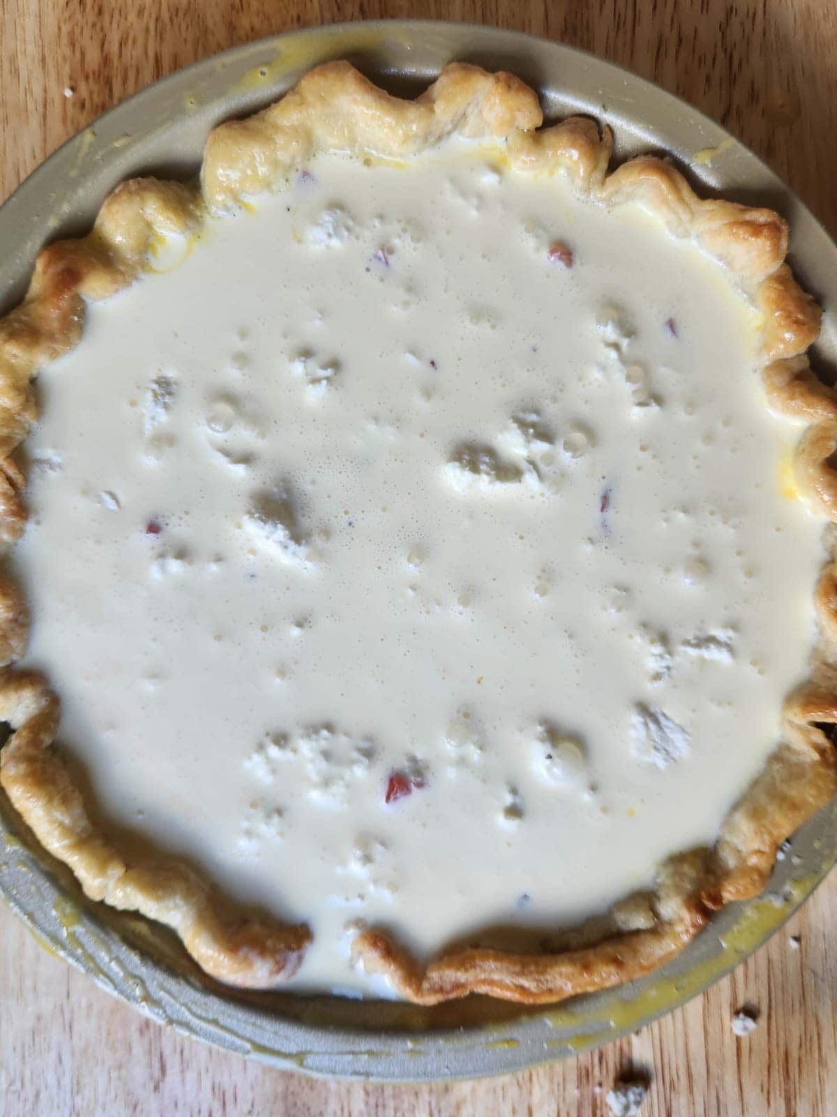Overhead of quiche custard in a metal pan with crust.