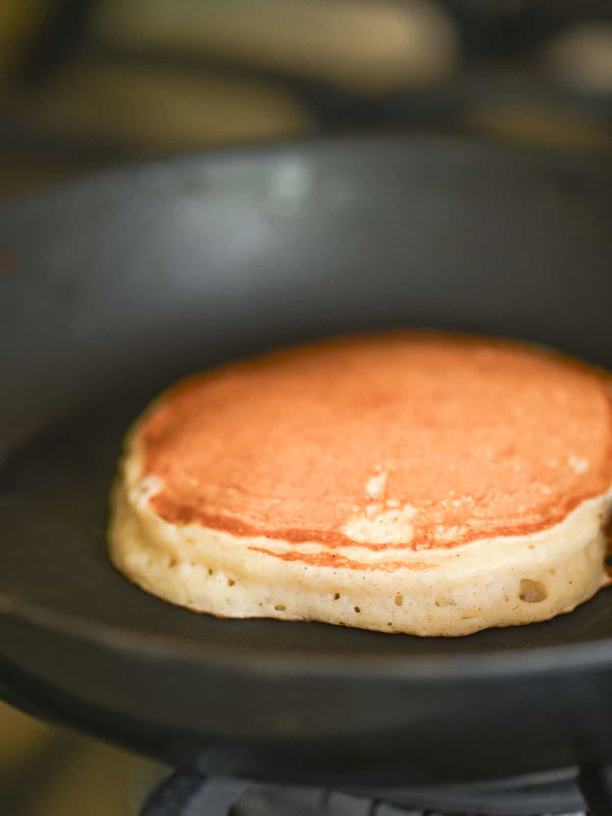 A pancake being cooked in a skillet showing how tall it is.