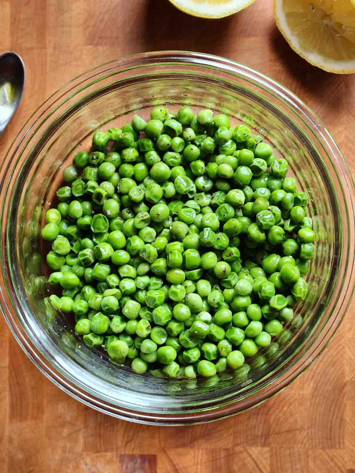 Overhead of seasoned peas in a clear bowl on a cutting board.