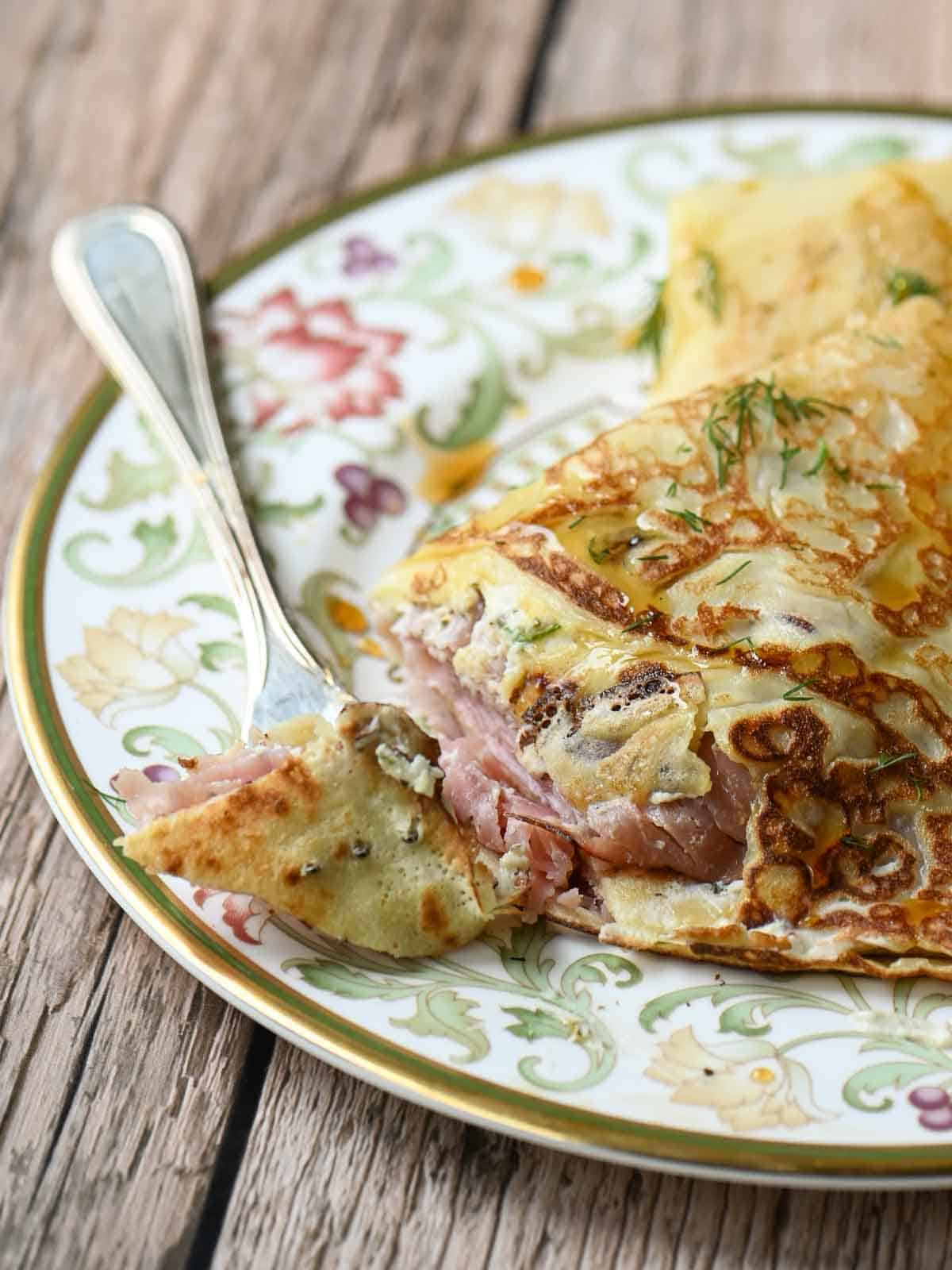 Savory crepes on a flowery plate with a fork to the left.