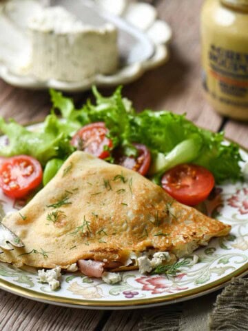 Savory crepes on a plate with a tomato and lettuce salad in the back.