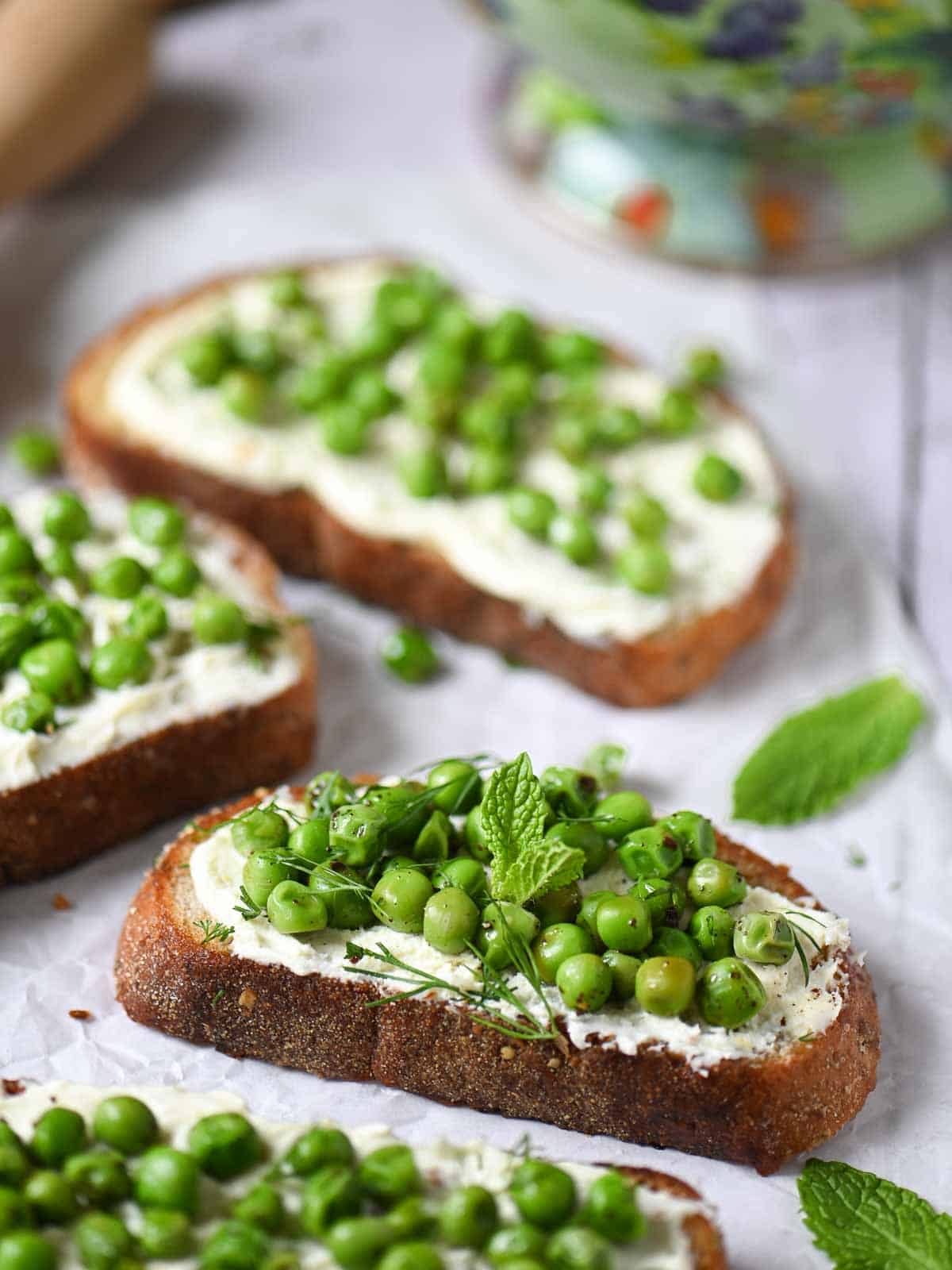Pea toasts with mascarpone and fresh herbs on a white board.