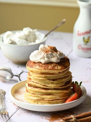 Whipped cream on top of a stack of fluffy pancakes.