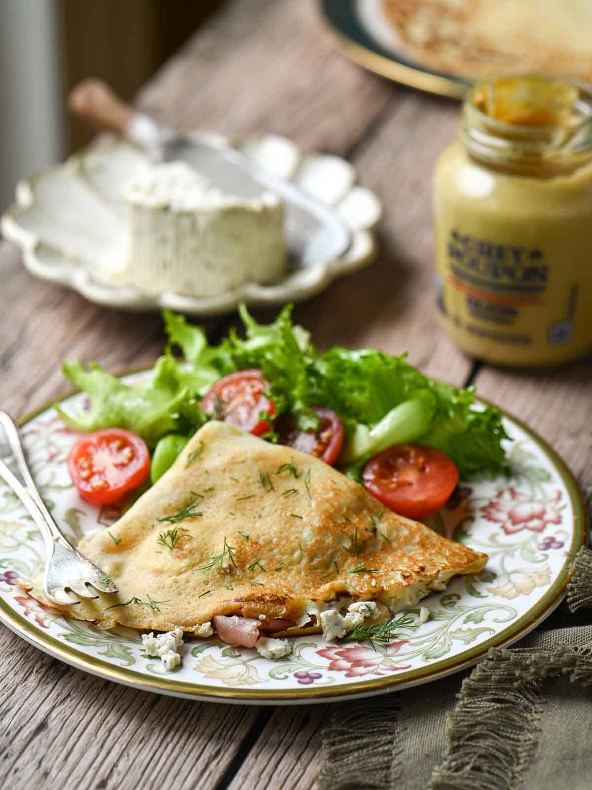 Savory crepes on a plate with a tomato and lettuce salad in the back.