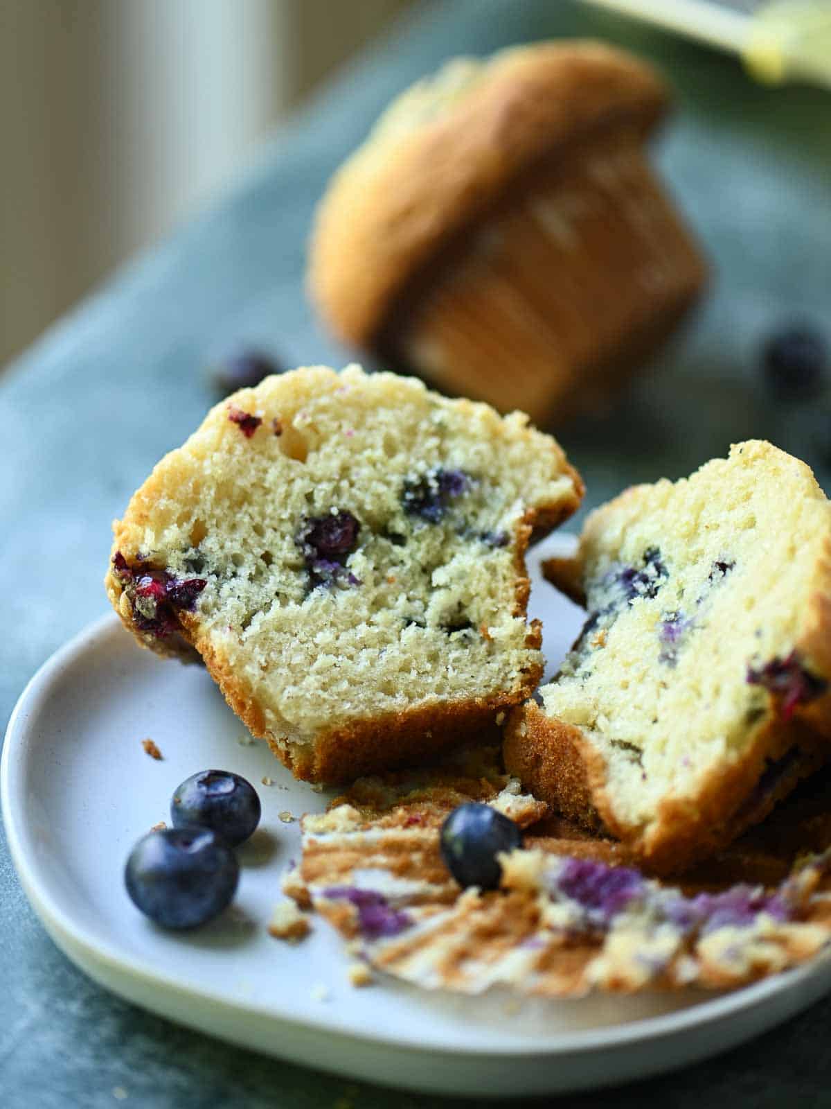A blueberry muffin sliced in half, showing the texture on a white plate.