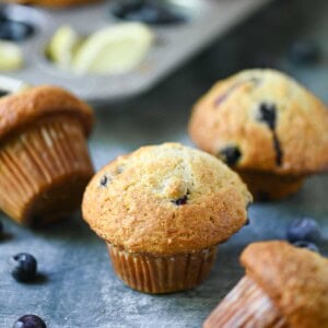 Scattered blueberry muffins in a muffin pan and on a blue surface.
