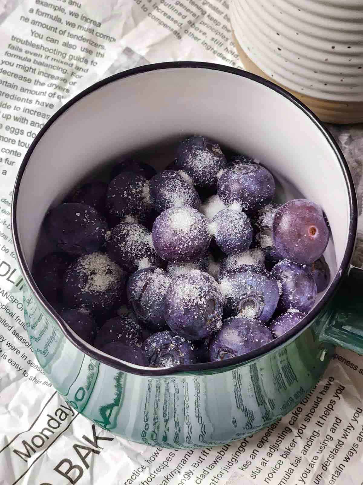 Blueberries and sugar in a small green pot.
